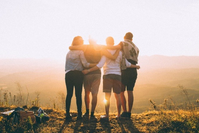 Vier Freunde stehen eng umschlungen im Licht es Sonnenuntergangs