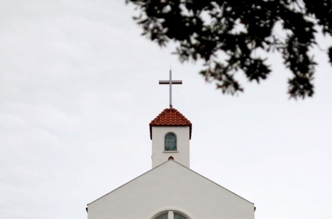 Eine Kirche hat eine weiße Fassade und ein Kreuz auf dem Turm