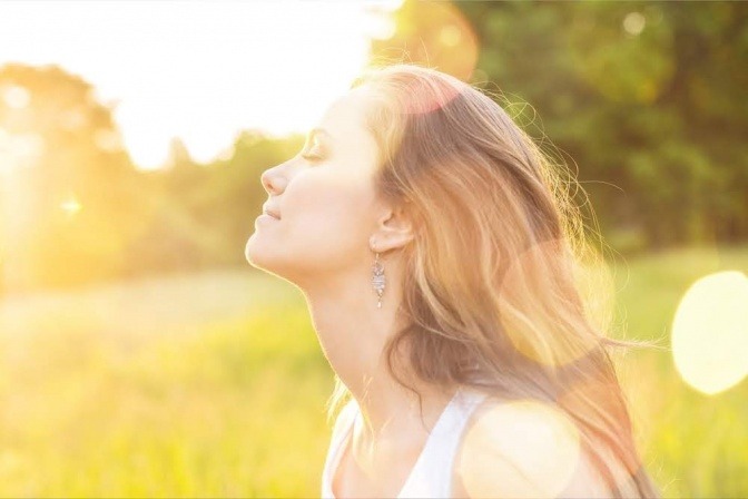 Eine Frau sitzt auf eine Wiese und lässt sich die Sonne ins Gesicht scheinen.