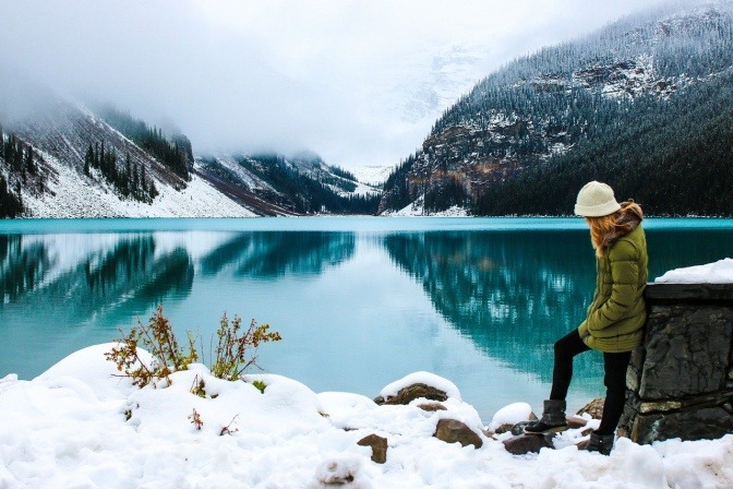 Eine Frau steht im Winter an einem See und übt sich in Achtsamkeit