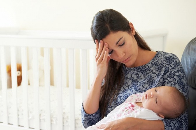 Eine Mutter sitzt mit ihrem Kind neben dem Kinderbett