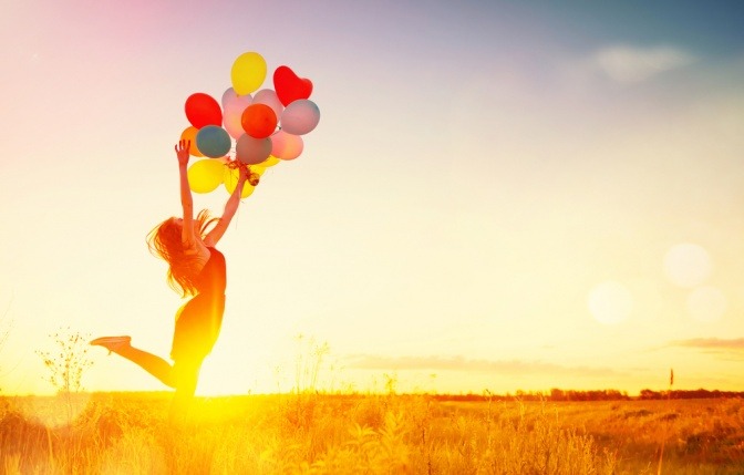 Glückliche Frau lässt während eines Sonnenuntergangs Luftballons in die Luft steigen.