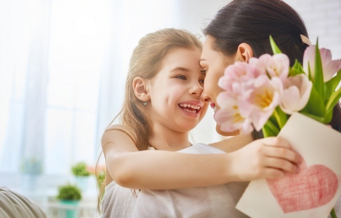 Eine Mädchen überreicht ihrer Mama Blumen und eine Grußkarte