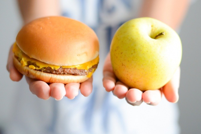 Eine Frau hält einen Burger in einer Hand, einen Apfel in der anderen