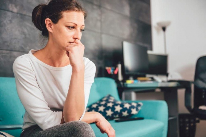 Frau, eventuell mit Burnout, sitzt grübelnd auf dem Sofa