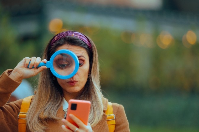 Frau benutzt Lupe, um etwas auf dem Smartphone genauer zu betrachten.