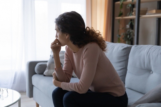 Nachdenkliche und besorgt wirkende Frau auf Sofa.