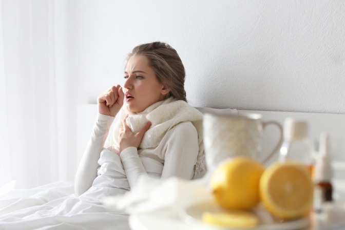 Frau hustet sitzend im Bett