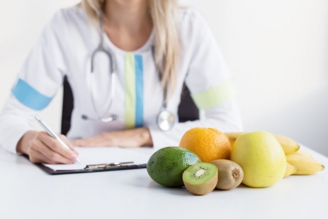 Eine Ernährungsexpertin sitzt vor einem Obstteller und schreibt etwas auf