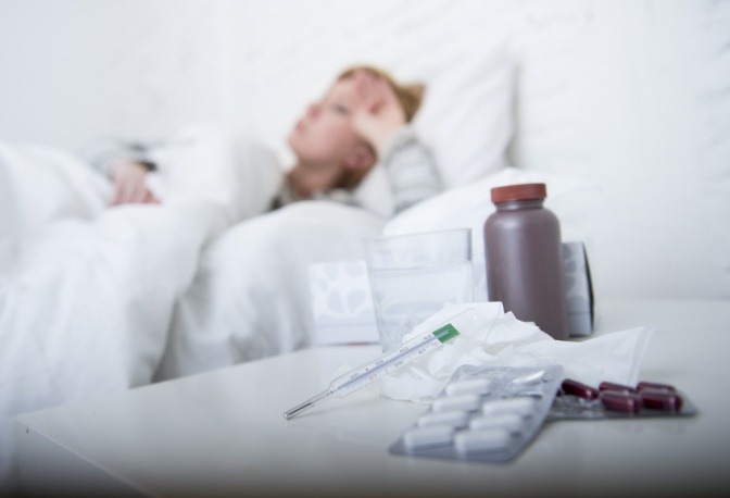 Eine Frau liegt im Bett, vor ihr stehen Medikamente