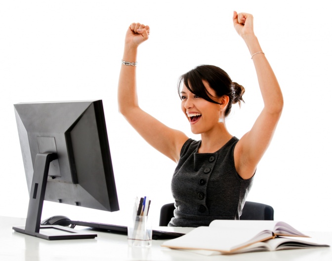 Eine Frau sitzt vor Überengagement als Burnout Phase 1 vor ihrem Computer und freut sich über ihre Arbeit.