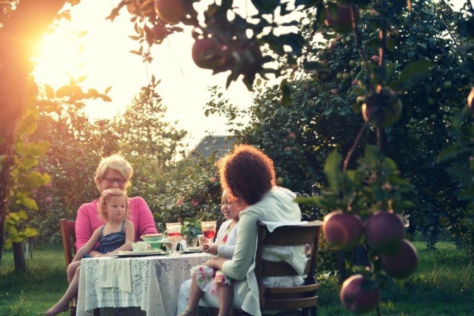 Im Garten zwischen Obstbäumen sitzt eine Familie mit Kindern auf Gartenmöbeln