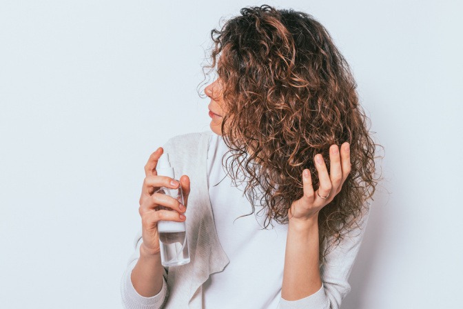 Frau mit lockigem Haar verwendet selbstgemachtes Haarspray. 