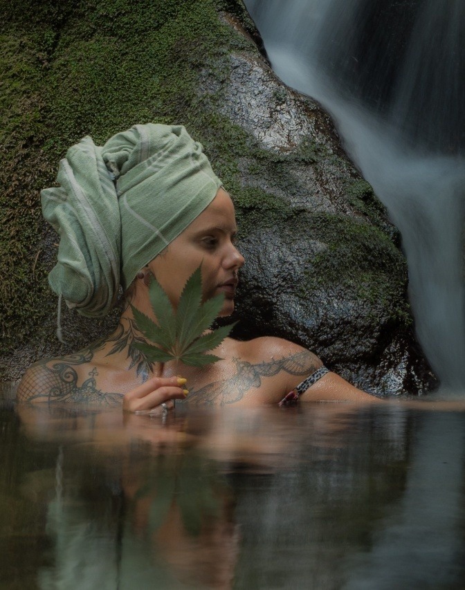 Eine Frau im Wasser hat ein Hanftuch am Kopf, ein Hanfblatt in der Hand