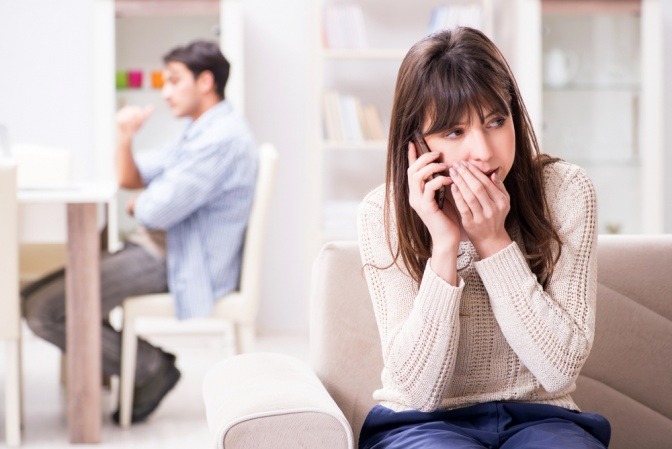 Eine Frau telefoniert heimlich, während ihr Partner im Hintergrund sitzt. 