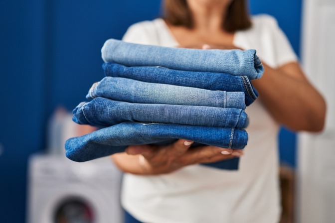 Frau hält einen Stapel gefalteter Jeanshosen in der Hand. 