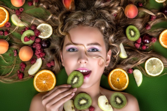 Junge Frau inszeniert mit Früchten in den Haaren. 