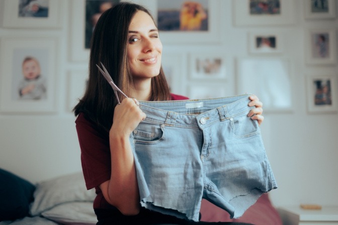 Kleidung aufpeppen Tipps - Frau hält selbstgemachte Jeans-Shorts hoch, die sie durch Upcycling einer alten Hose hergestellt hat.