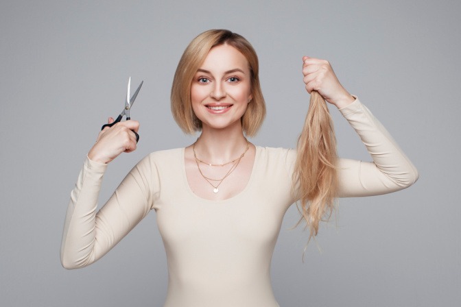 Frau mit Slob hält Schere und lange Haare in der Hand