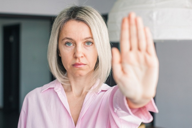 Frau zeigt abwehrende Haltung mit erhobener Hand und gestrecktem Arm.