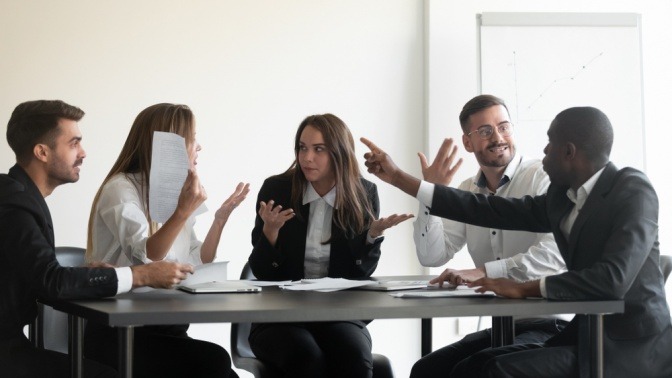 Eine Gruppe von Mitarbeitern streitet sich lautstark in einem Konferenzraum.