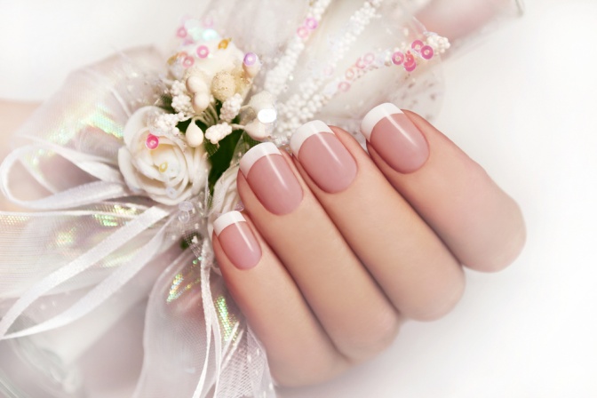 Eine Hand mit nude und french lackierten Nägeln hält Nagellack