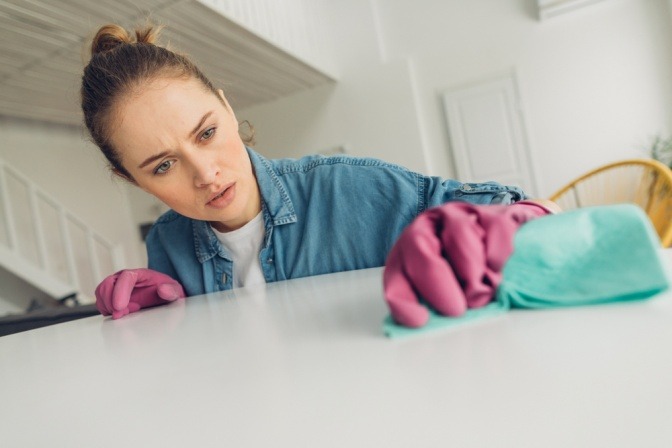 Porträt einer gewissenhaften jungen Frau, die zu Hause sorgfältig die schmutzigen Flecken auf einem Tisch abwäscht.