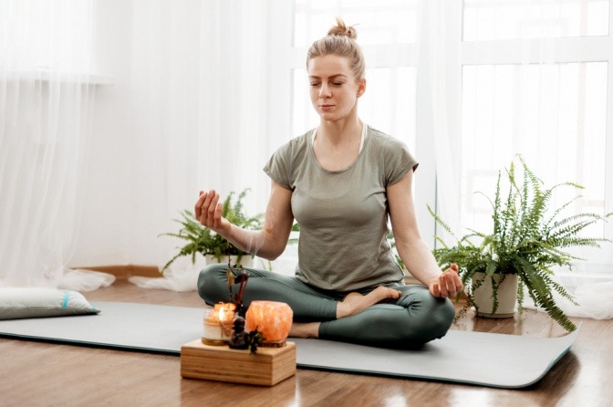 Frau macht Yoga und hat dabei eine Räucherkerze brennen.