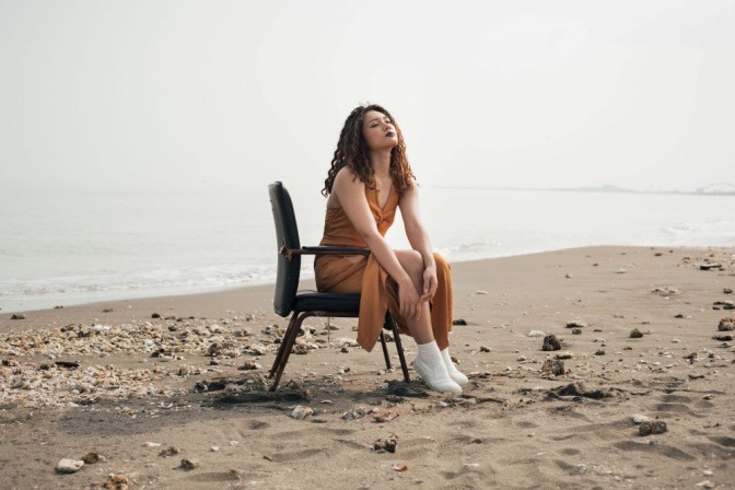 Eine Frau sitzt am Strand in einer wenig rückenfreundlichen Körperhaltung