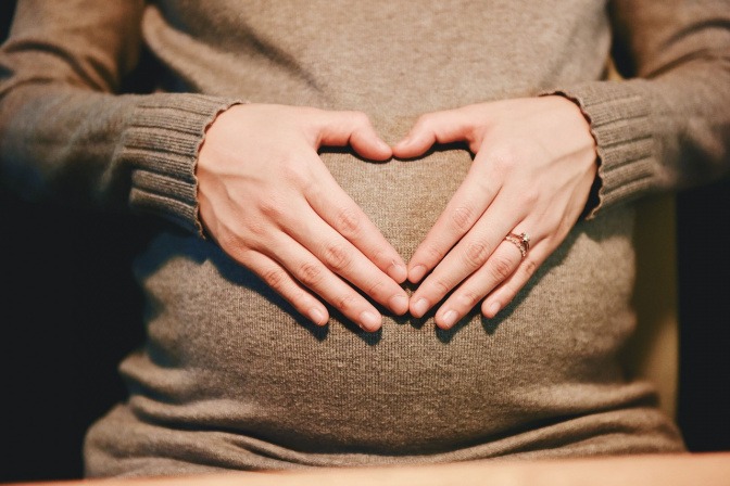 Schwangere Frau formt mit ihren Händen auf dem Bauch ein Herz