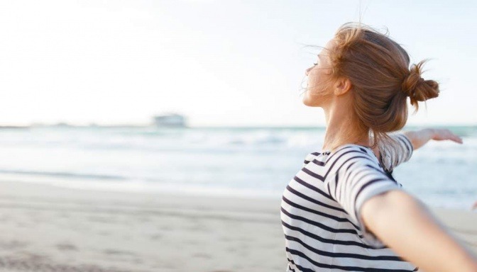 Frau mit ausgebreiteten Armen am Meer.