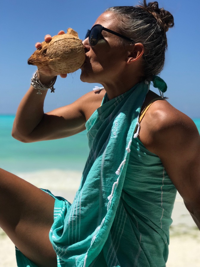 Eine Frau in einem Tuch als Strandkleid trinkt aus einer Kokosnuss