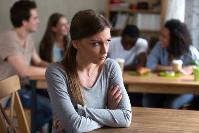 Nach einem Streit mit ihren Freunden sitzt eine Frau einsam am Tisch, während ihre Freunde hinter ihr sitzen und eine gute Zeit haben.