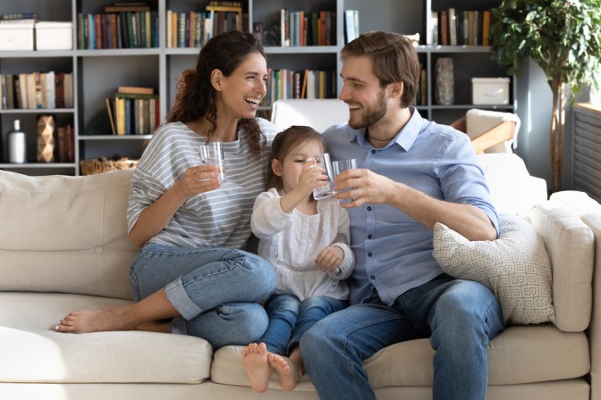 Eine Familie sitzt auf dem Sofa und alle trinken Wasser aus Gläsern.