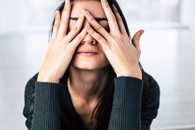 Eine Frau stützt ihren Kopf auf die Hände und zeigt Symptome von Stress