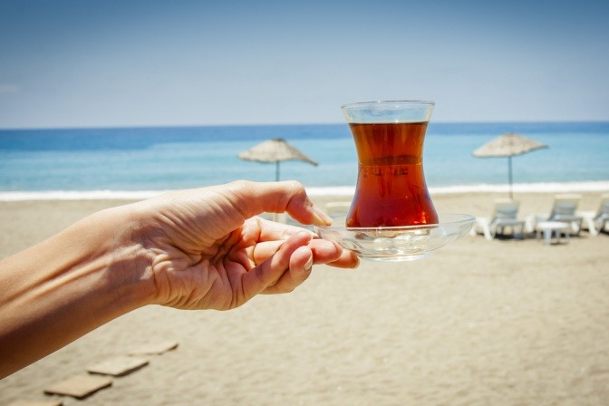 Eine Hand hält eine Tasse Tee im Sommer am Strand