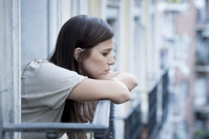 Eine Frau blickt traurig wegen Isolation von ihrem Balkon