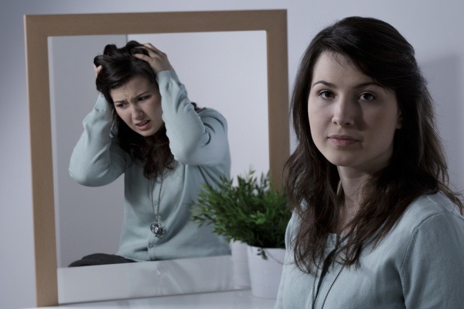 Frau hat einen fröhlichen Gesichtsausdruck, ihr Spiegelbild zeigt sie jedoch verzweifelt und unzufrieden.