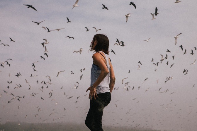 Durch viele Vögel scheint ein Chaos am Himmel zu sein. Eine Frau steht darunter