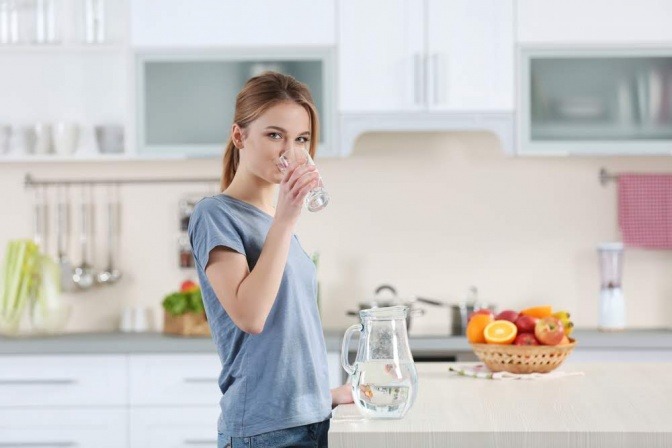 Eine Frau trinkt Wasser als Unterstützung zum Heilfasten, Entschlacken 