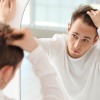 Mann betrachtet sich im Spiegel und macht sich Gedanken über Kosten einer Haartransplantation