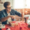 Geschenke originell verpacken Tipps - junger Mann verpackt Präsente auf Tisch.