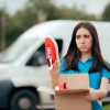 Frau mit enttäuschtem Gesichtsausdruck läuft mit einem Karton mit Schuhen, die quietschende Sohlen haben, durch die Gegend. 