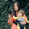 Stress durch Handy - Mutter mit Baby im Arm blickt gestresst auf ihr Smartphone.