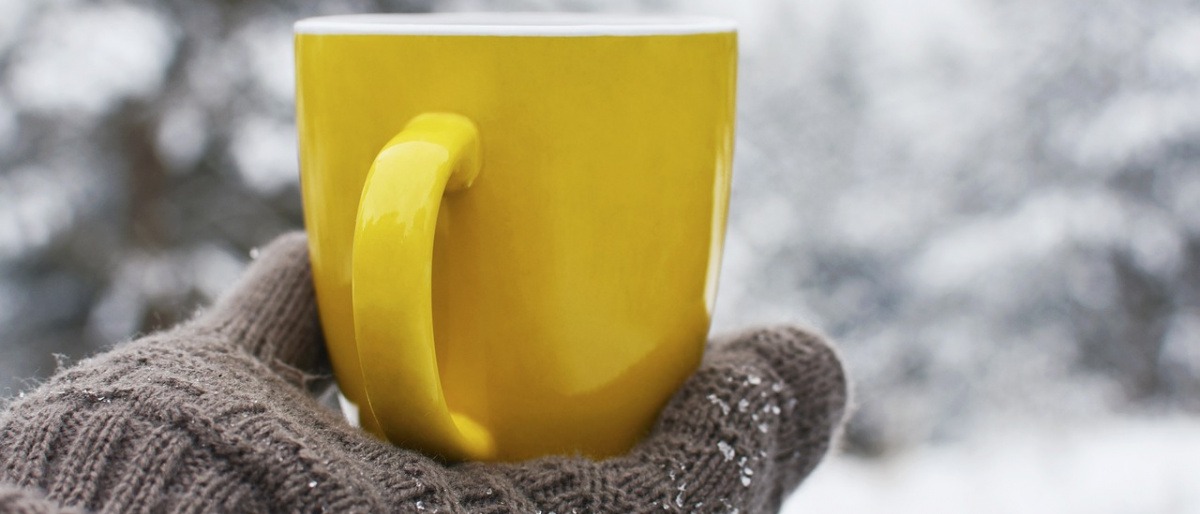 Frau mit Hanschuhen im Winter hält Teetasse in der Hand