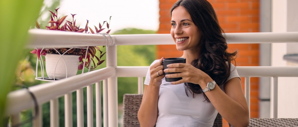 Lächelnde Frau sitzt am Balkon mit einer Tasse Tee