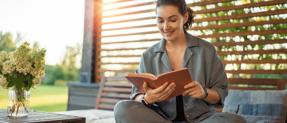 Eine Frau nimmt sich auf der gemütlichen Terrasse eine Auszeit und liest ein Buch