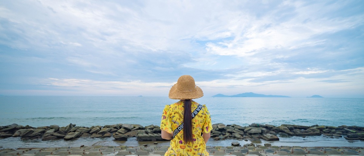 Frau in einem modischen Kleid sitzt am Meer