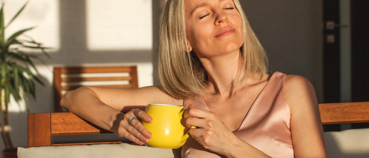 Frau mittleren Alters wird von der Sonne angestrahlt und wirkt zufrieden