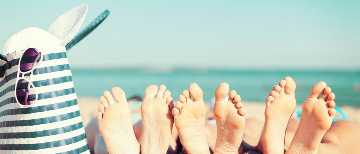 Füße liegen am Strand neben einer Badetasche